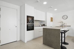 A modern kitchen with white cabinetry, a built-in oven, and a small island with bar stools.