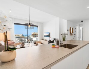 A modern kitchen with a large island, a dining area with a view, and a living space with a sofa and a plant. - Mimosa | Sea views - terrace (Fuengirola)