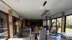A modern living room with a wooden dining table, comfortable seating, and large windows offering a view of the outdoors. - Villa des chateaux du pessac leognan (Martillac)