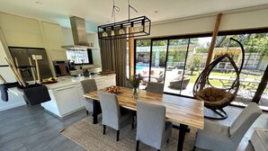 A modern kitchen with a dining area, large windows, and a hanging chair. - Villa des chateaux du pessac leognan (Martillac)