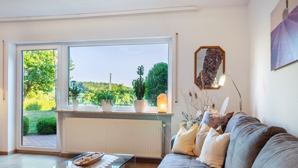Una sala de estar moderna con un sofá, una mesa de centro de vidrio, vistas a través de amplios ventanales y un radiador.