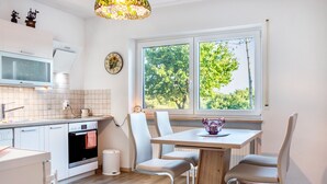 Una cocina moderna con armarios blancos, horno integrado, microondas y un comedor con mesa y sillas de madera.