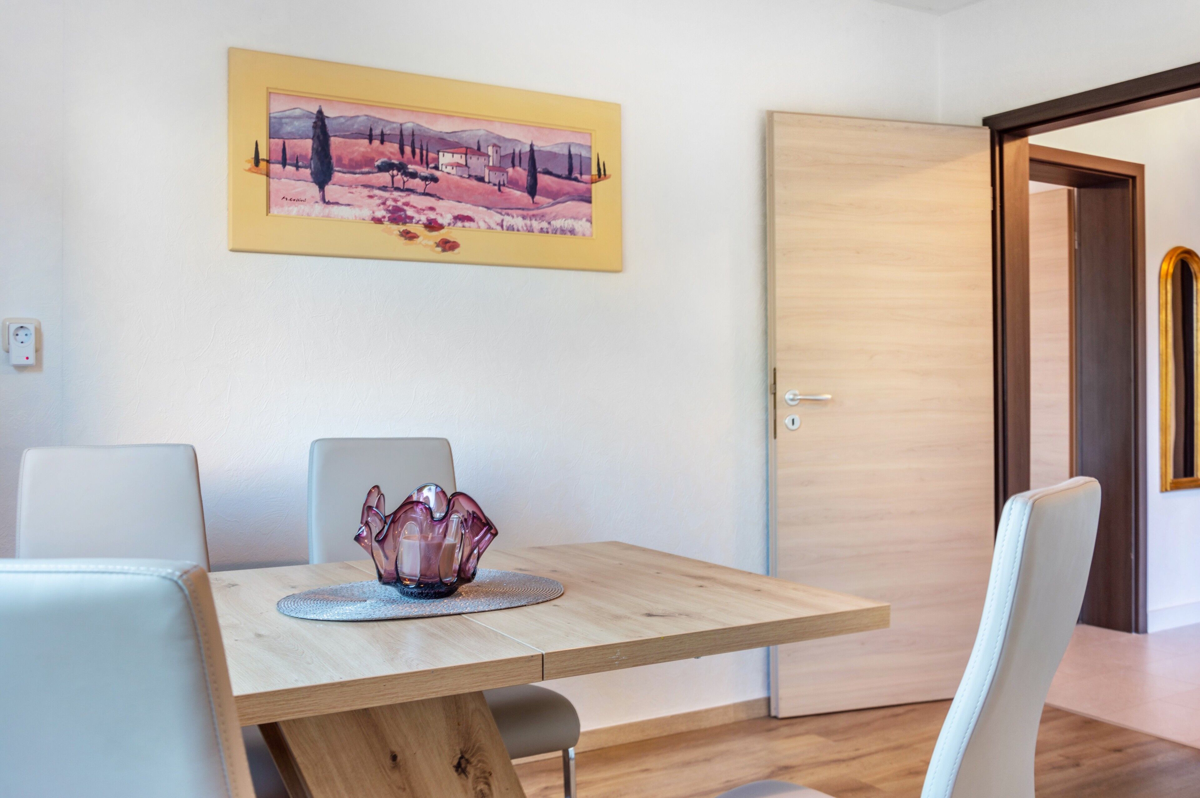 Un coin repas avec une table en bois, des chaises blanches et un objet décoratif en verre.