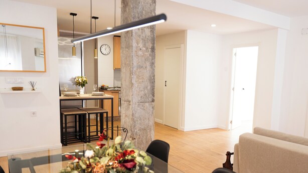 Een moderne woonkamer met een glazen eettafel, een beige bank en een keuken op de achtergrond.