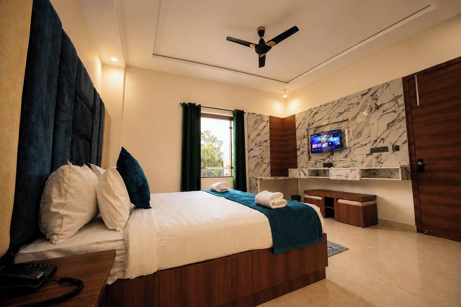 Een moderne hotelkamer met een bed, bureau, televisie en plafondventilator.