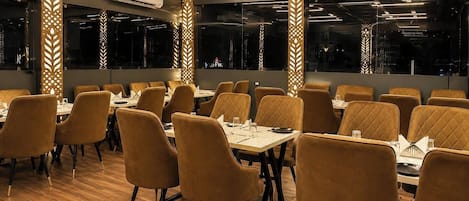 A restaurant interior with wooden flooring, cushioned chairs, and tables set for dining.