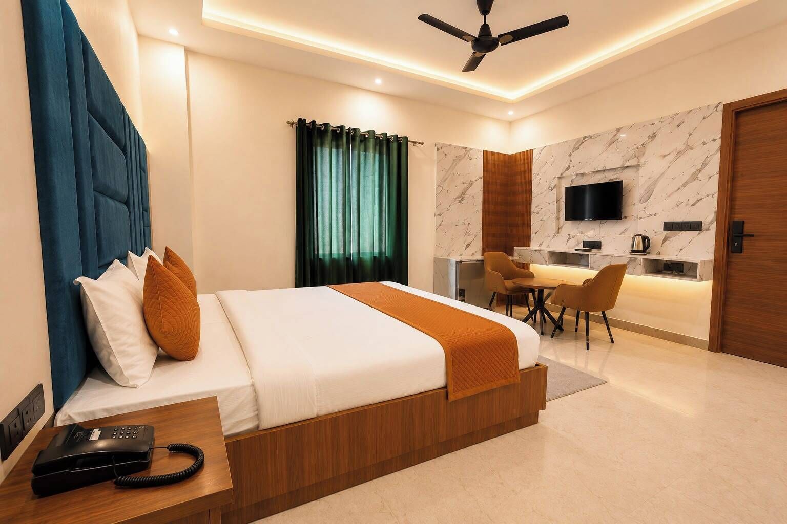 A modern hotel room with a bed, bedside table, and a desk area with chairs.