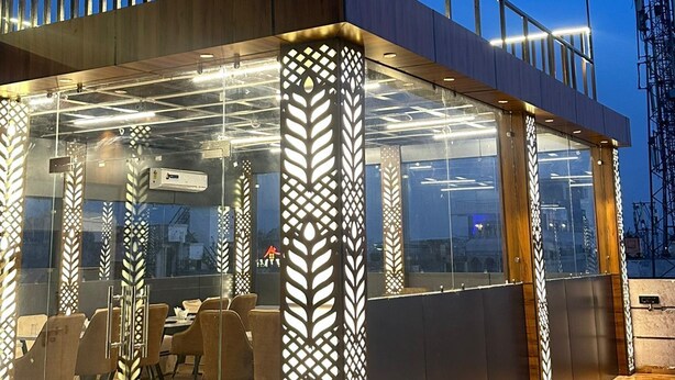 A modern outdoor seating area with glass partitions, wooden flooring, and a metal railing.