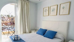 A neatly made bed with blue pillows and a blue throw blanket, a white bedside table, and a small nightstand. There are three framed pictures on the wall above the bed.