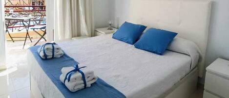 Un letto rifatto con cuscini e una coperta blu, un comodino bianco e un piccolo tavolino da notte. Sopra il letto, tre quadri appesi al muro.