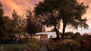 A house with a garden pathway leading to a white building, surrounded by trees and various plants.