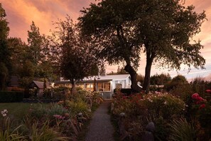 Una casa con un camino de jardín que lleva a un edificio blanco, rodeada de árboles y plantas diversas.
