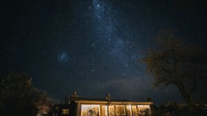 A house with large windows, a visible chimney, and a starry night sky.