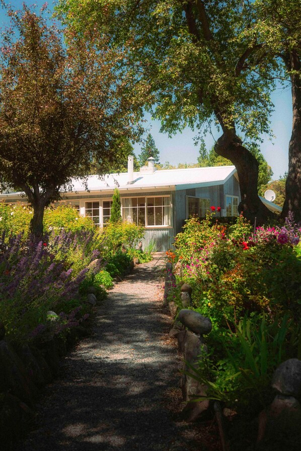A pathway leading to a house surrounded by lush greenery and flowering plants.