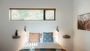 Un dormitorio con cama, una ventana, dos mesitas de noche y una estantería en la pared.