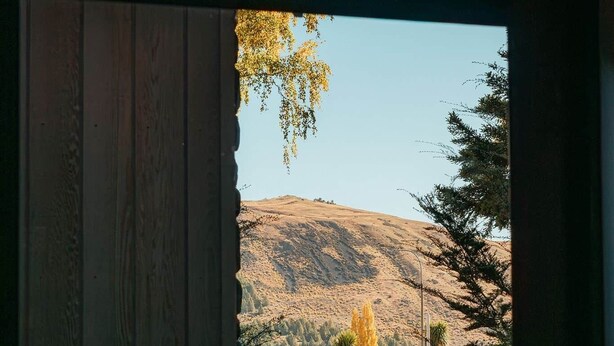 Vista a través de una puerta de madera, mostrando un paisaje montañoso con cielo despejado.