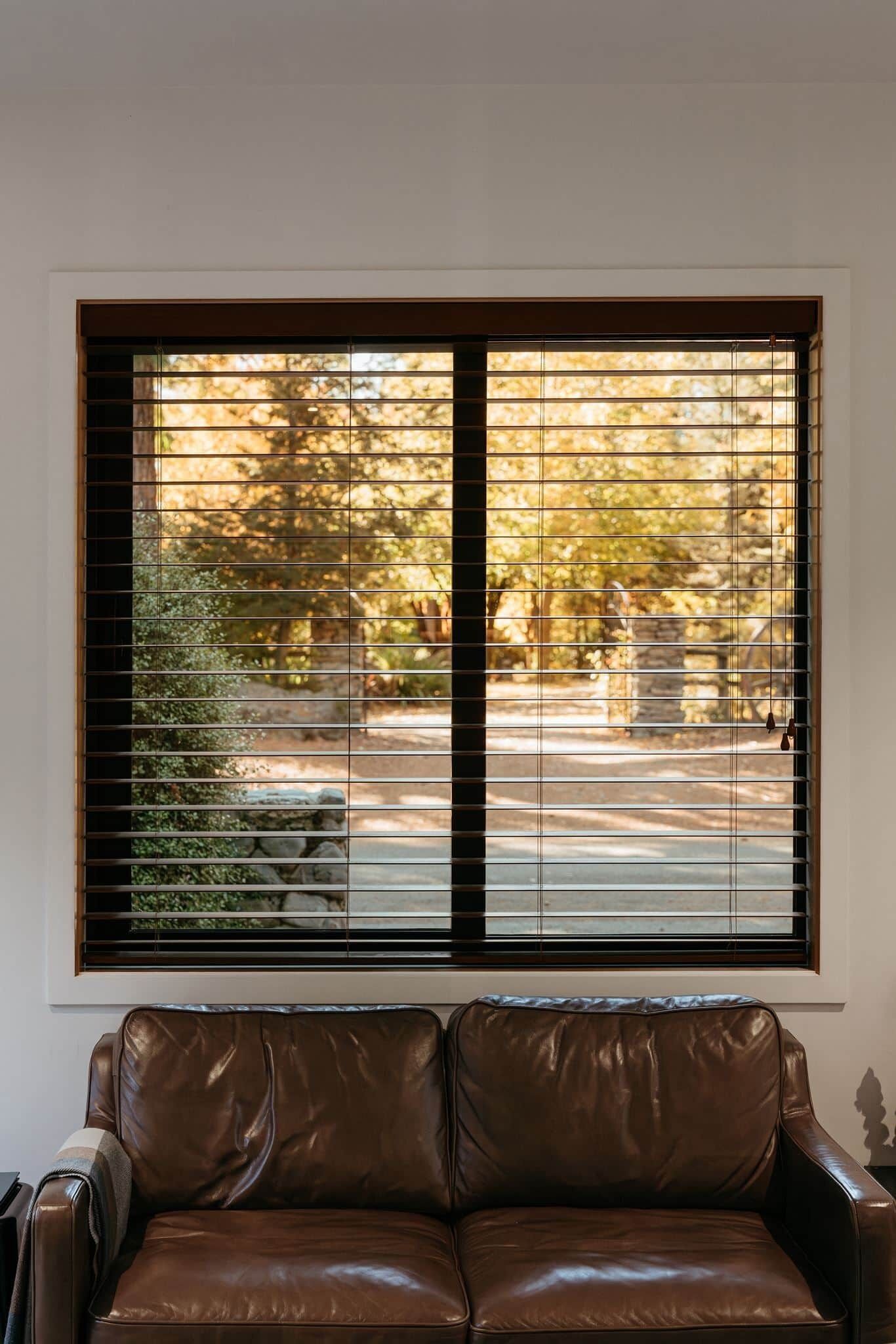 Ein Zimmer mit einem braunen Ledersofa und einem Fenster mit Jalousien.
