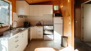 A compact kitchen with white cabinets, a stainless steel sink, a stove, and a microwave. - Awa Cottage - Lake Tekapo (Lake Tekapo)