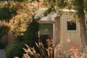 A wooden signboard for AWA COTTAGE, a holiday accommodation, with contact details and a website URL.