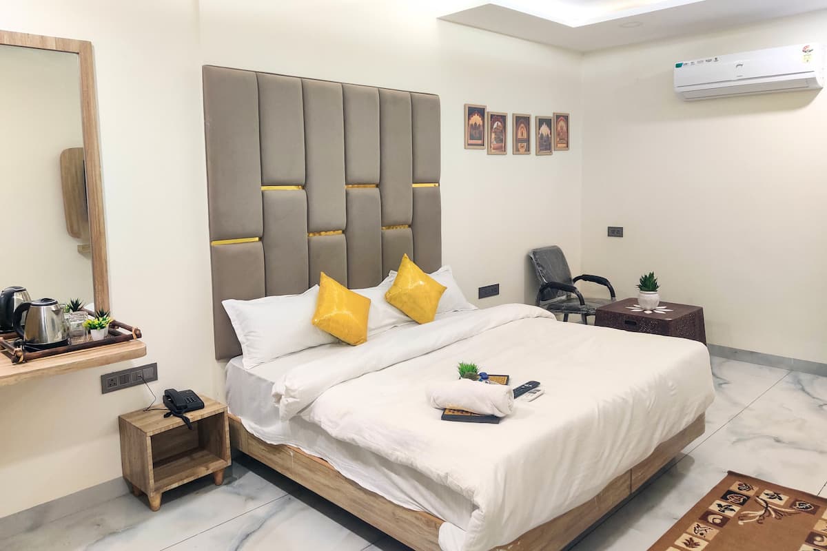 Une chambre d’hôtel moderne avec un grand lit, une table de chevet avec un téléphone, une petite table d’appoint avec une plante et un ventilateur de plafond.