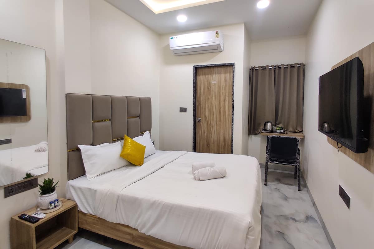 Une chambre d’hôtel moderne avec un grand lit, une table de chevet avec une télécommande, une petite plante et un téléviseur fixé au mur.