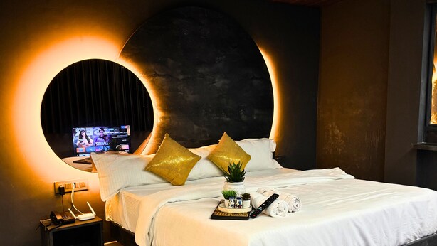 Un dormitorio moderno con una cama grande, un espejo redondo y un televisor en la pared.