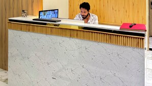 Un mostrador de recepción con encimera de mármol, un monitor de computadora y una carpeta roja.