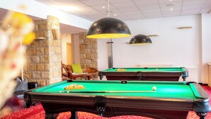 A pool table area with two pool tables, a stone wall, a green sofa, and a red patterned carpet. - AaRa Hotel (Radeberg)