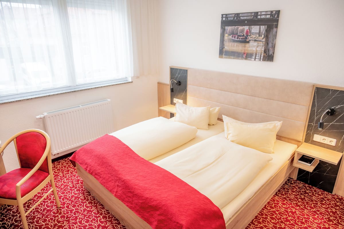 A hotel room with a double bed, a red chair, a small bedside table, and a wall-mounted artwork.