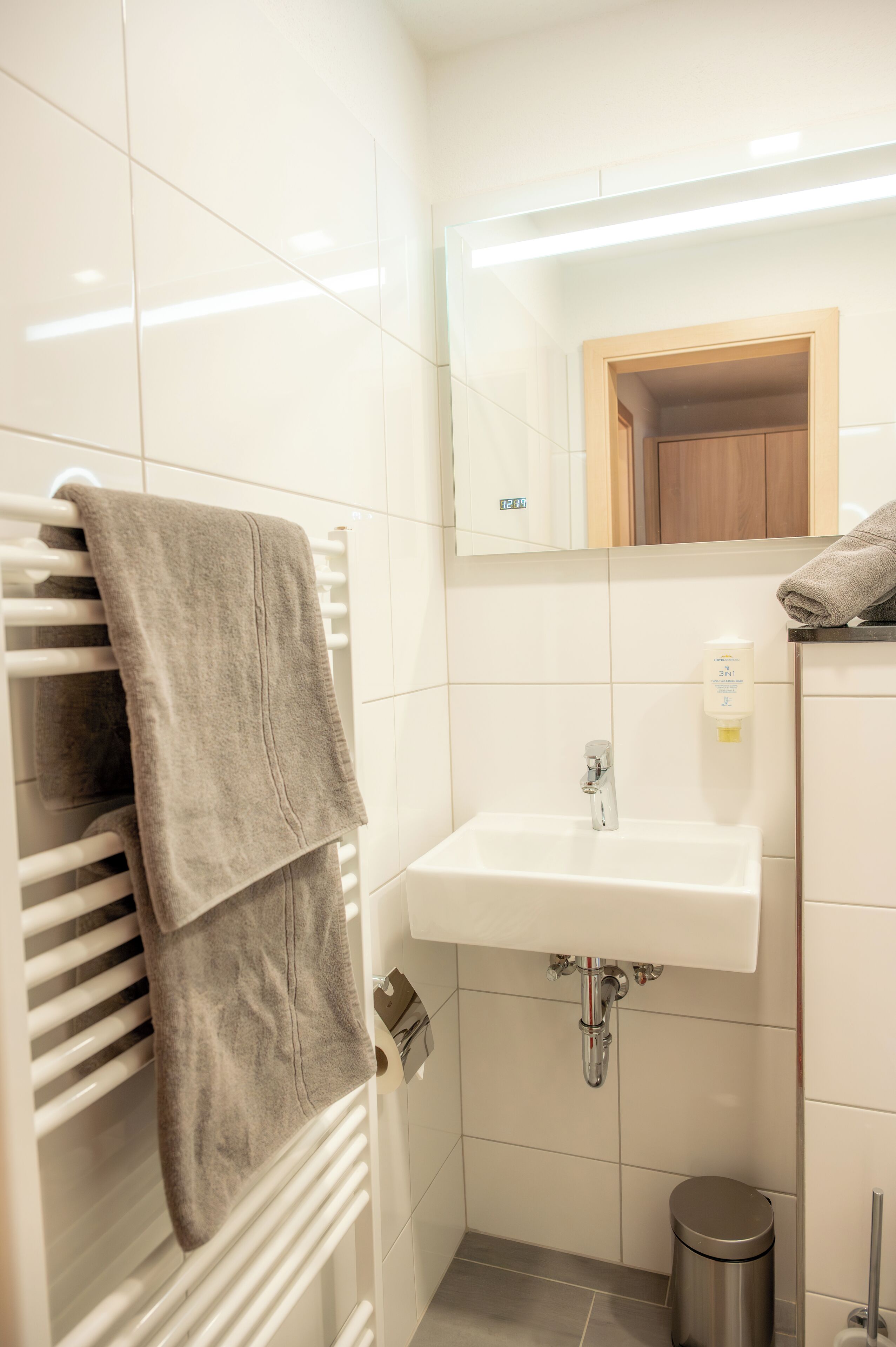 A bathroom with a white sink, a mirror, a towel rack, and a trash bin.