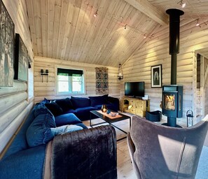 A cozy cabin interior with a wooden log wall, a sofa, a TV, a fireplace, and a dining area. - Indoor hot tub, views & nature, cosy family cabin (Vang kommune)