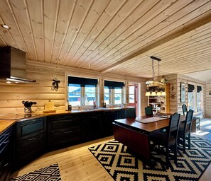 A log cabin interior with a kitchen and dining area, wooden ceiling, and large windows. - Indoor hot tub, views & nature, cosy family cabin (Vang kommune)