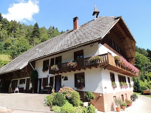 A traditional chalet with a steep roof, wooden balconies with flower boxes, and a stone chimney. - Bright Room with Green Views, Balcony, and Pets on Request (Hornberg)