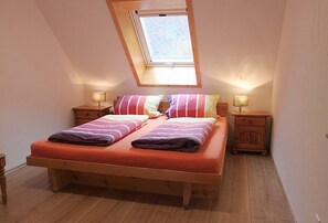 A bedroom with a sloped ceiling, a skylight, a double bed with striped bedding, two bedside tables with lamps, and wooden flooring.