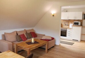 A cozy living area with a sofa, a wooden table, and a kitchen with white cabinets and appliances.