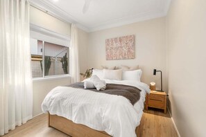 A bedroom with a bed, a nightstand, a window with curtains, and a wall-mounted artwork. - B's Beach House - Beachfront (AVOCA BEACH)