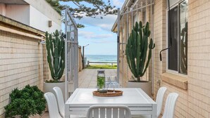 Een terras met tafel en stoelen, een cactussplant en uitzicht op de oceaan.
