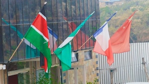 Flags hanging outside a building with a metal fence and a hillside in the background. - Home of Comfort (Narok County)
