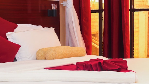 A neatly made bed with white and red bedding, a beige throw pillow, and a canopy. - Home of Comfort (Narok County)