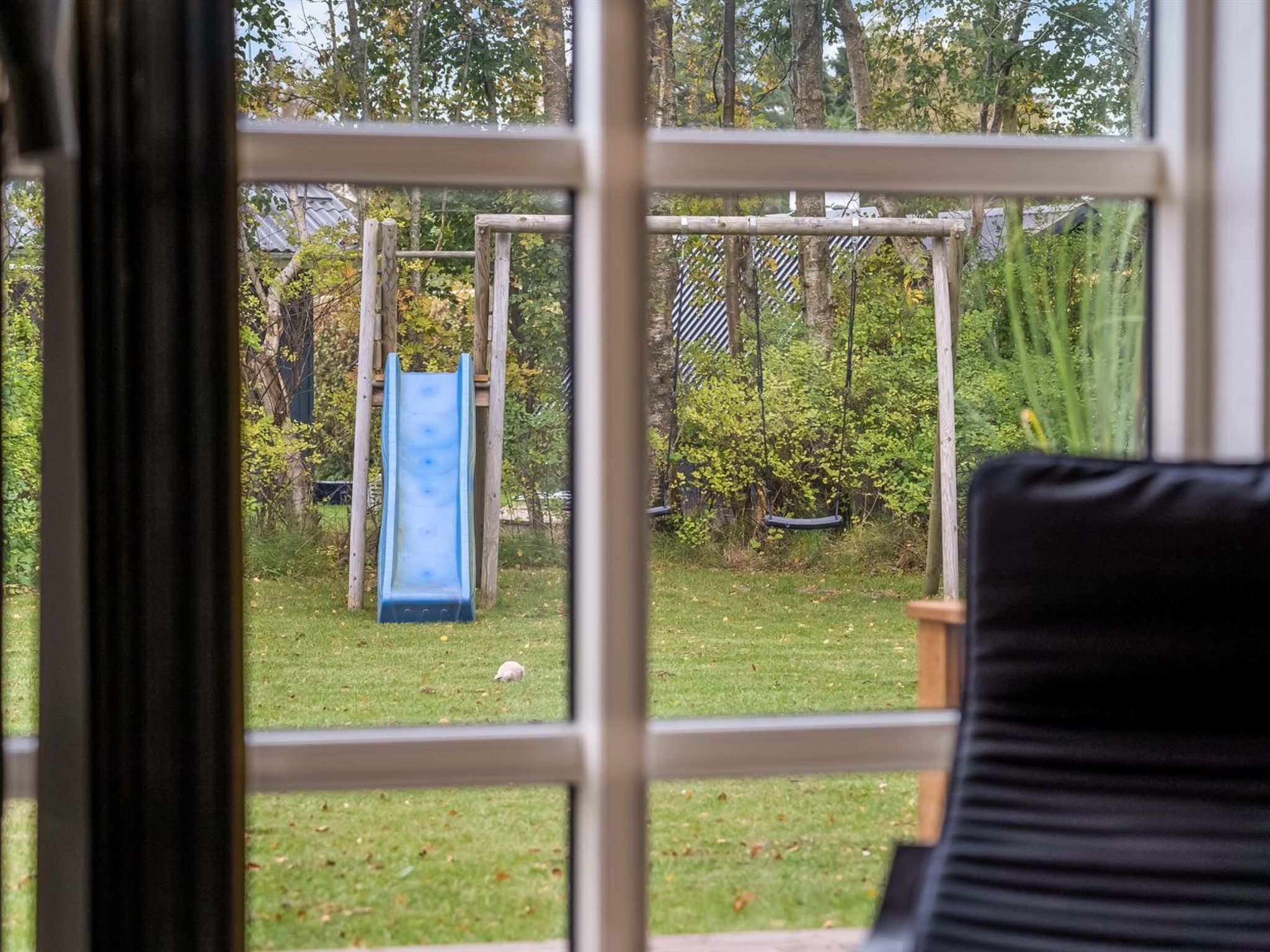 A view through a window of a backyard with a wooden swing set and a blue slide.