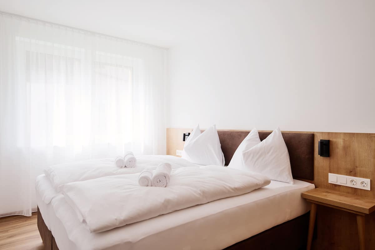 A neatly made bed with white linens and pillows, a wooden headboard, and a bedside table with a power outlet.