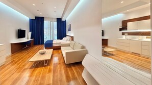 A modern hotel room with a wooden floor, a sofa, a bed, a desk, and a kitchen area. - Condo Studio Plaza (Budva)