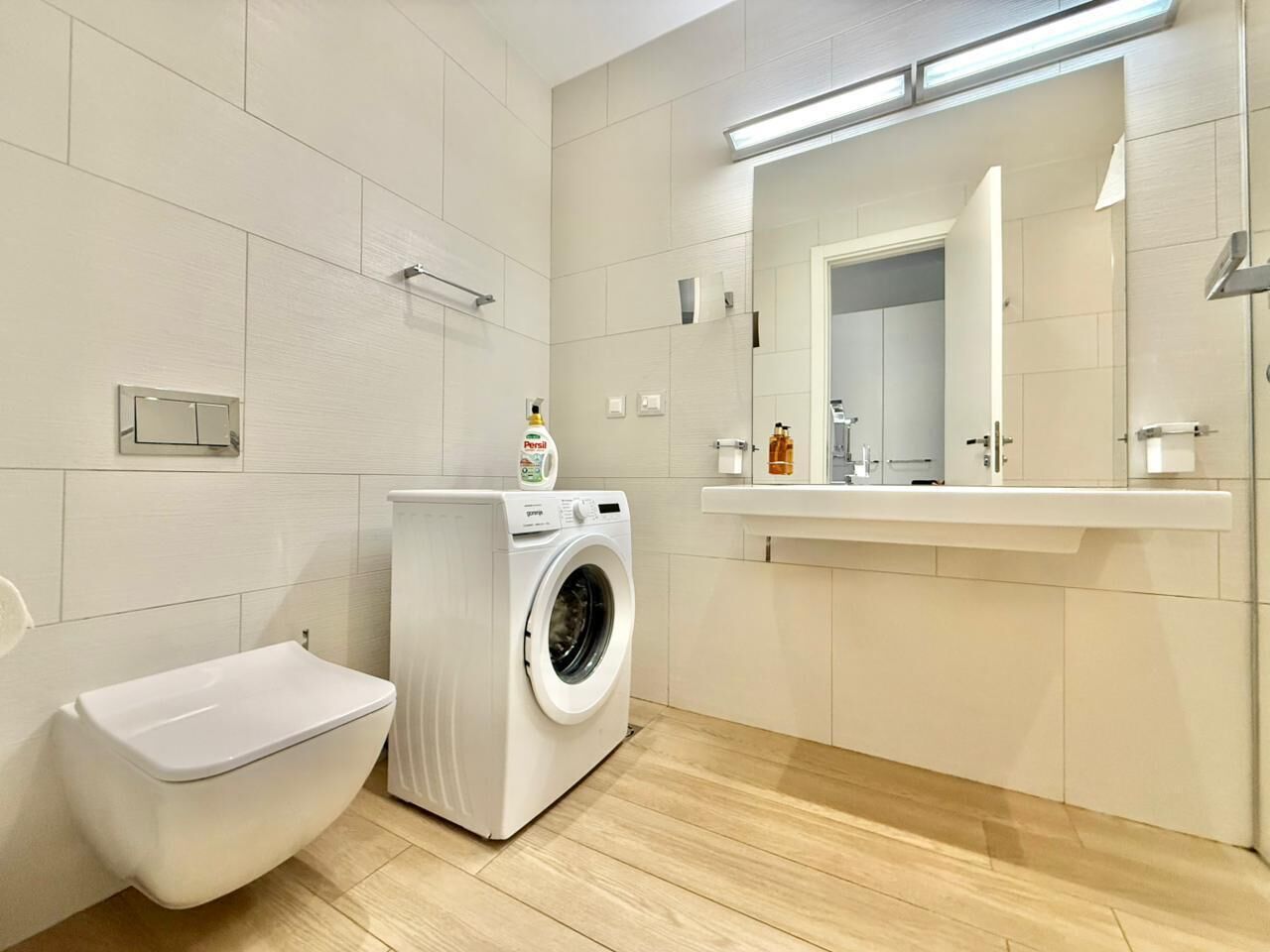 A modern bathroom with a toilet, washing machine, and a large mirror above the sink.