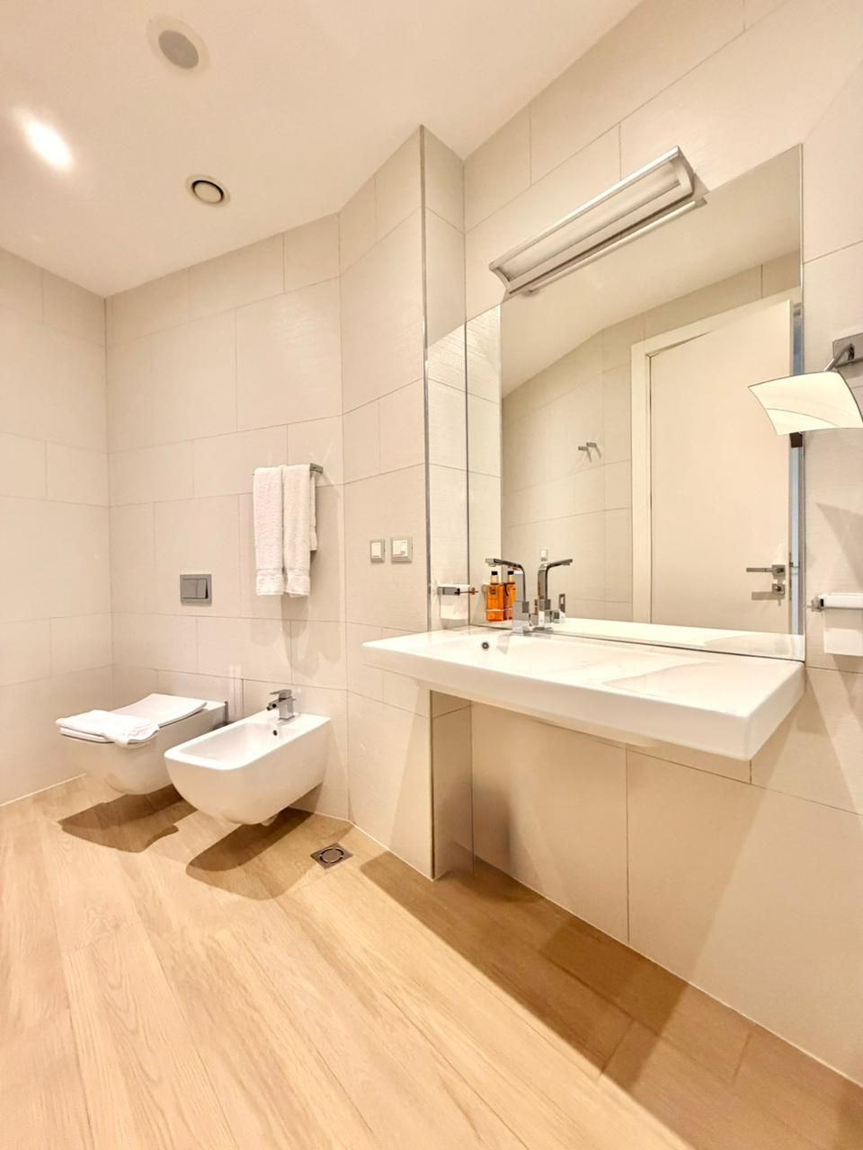Un baño moderno con un espejo grande, un bidé, un lavabo y un inodoro.
