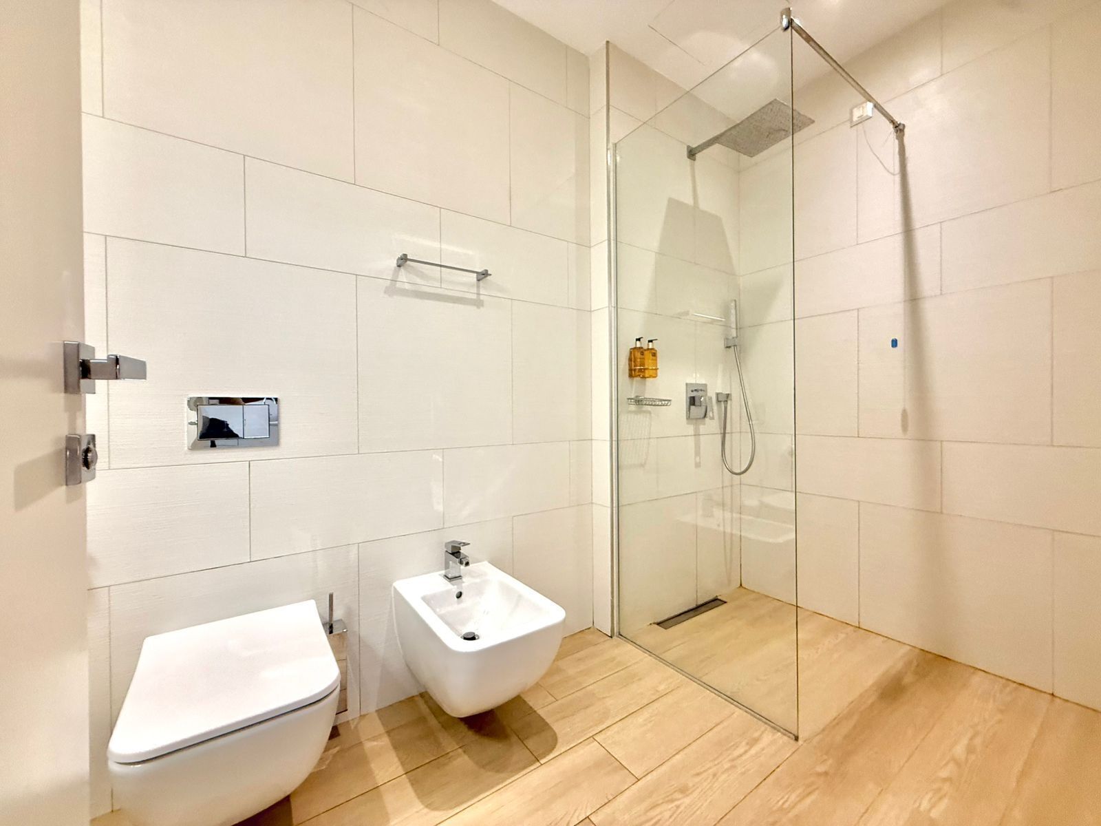 A modern bathroom with a glass-enclosed shower, a white toilet, and a bidet.