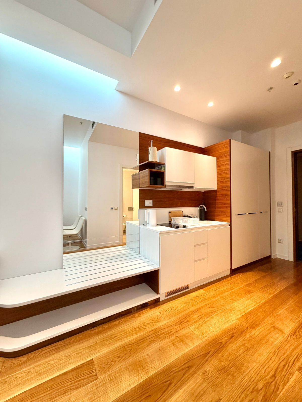 A modern kitchen with white cabinetry, a wooden accent wall, and a built-in bench.