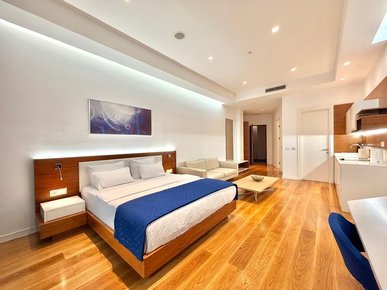 Una habitación de hotel moderna con una cama de madera, una mesita de noche, un escritorio pequeño y una silla.