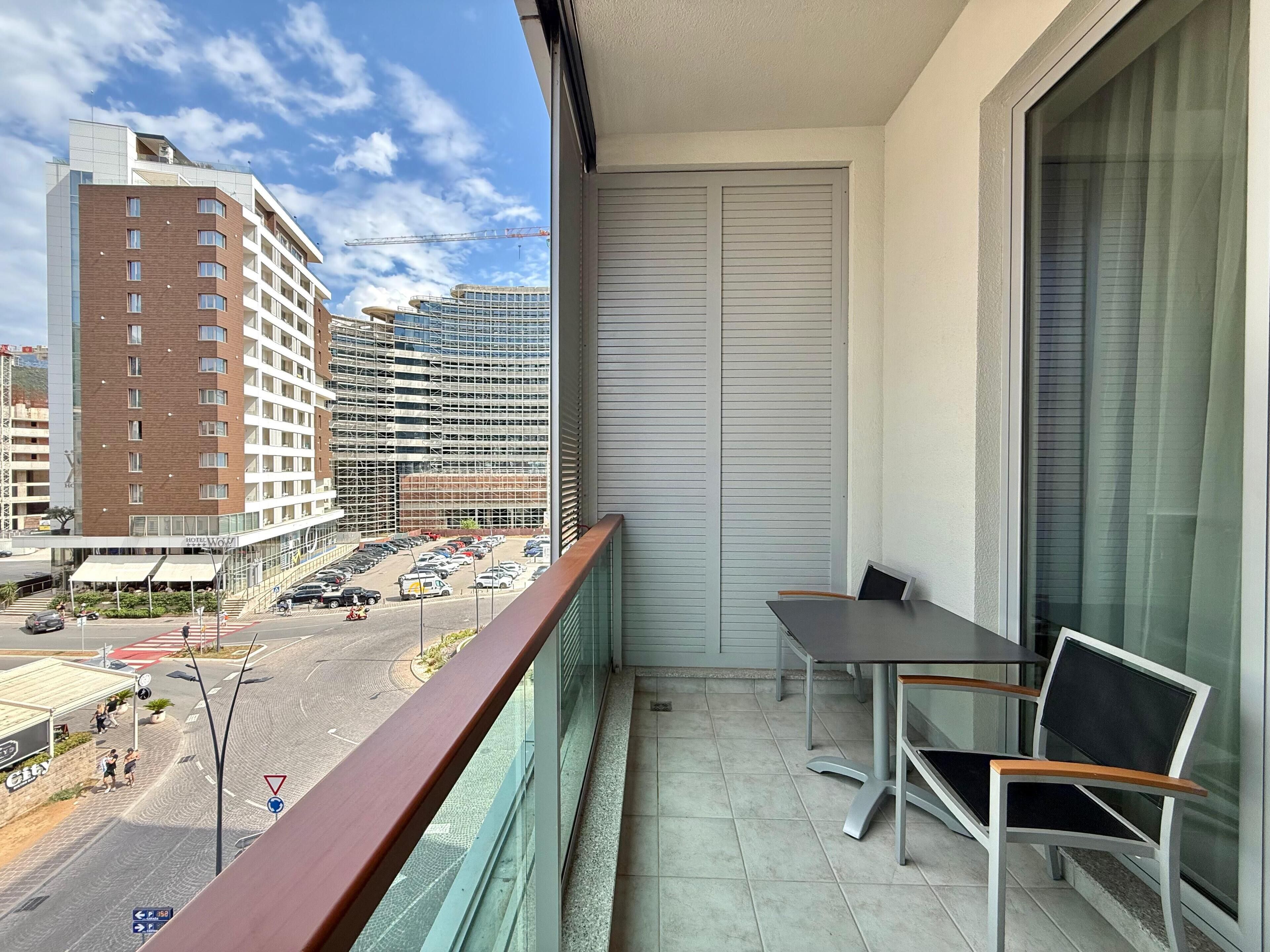 A balcony with a table and chairs, overlooking a parking area and buildings.