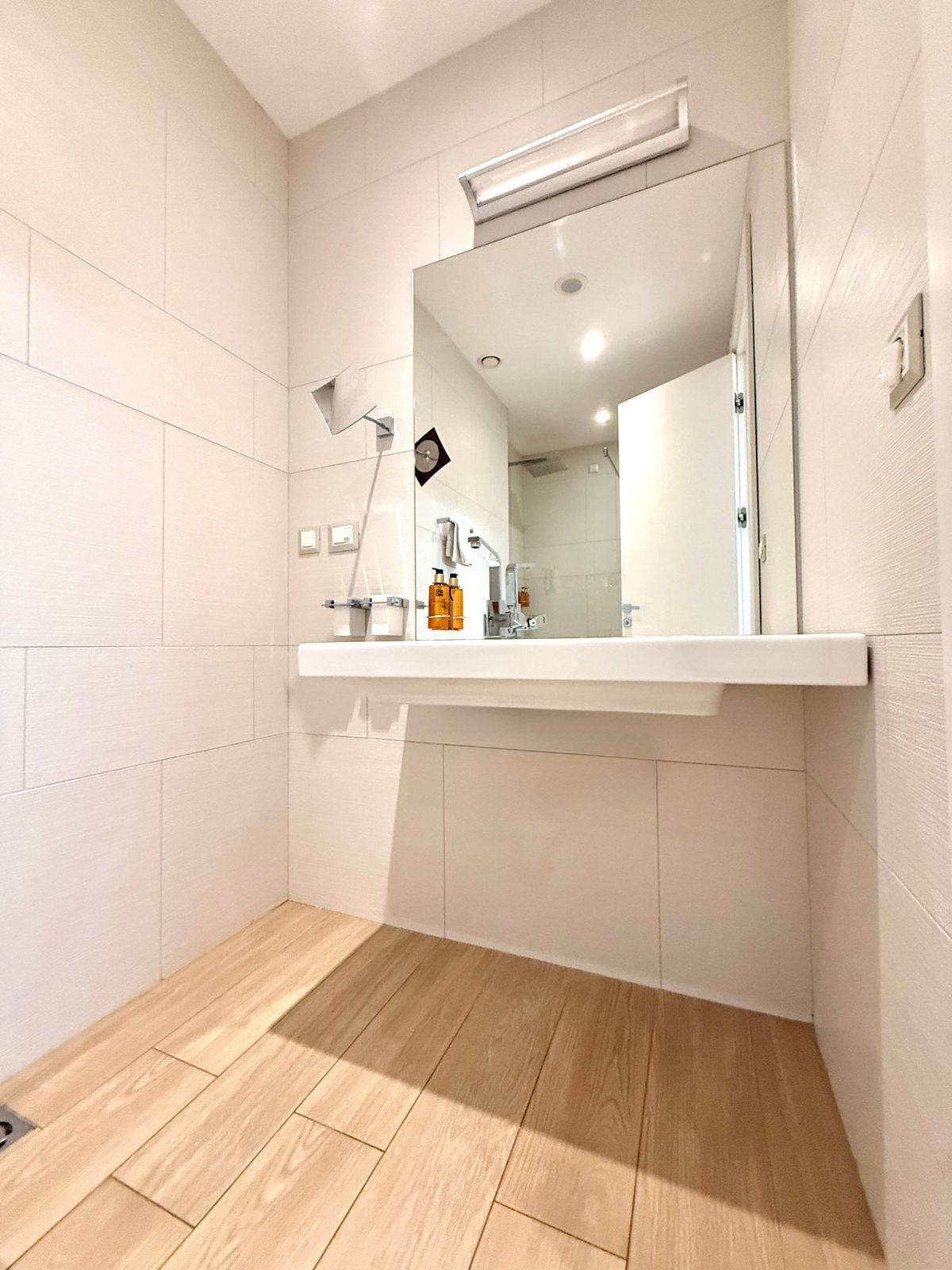 Une salle de bain moderne avec un grand miroir, des carreaux blancs et un plancher en bois.