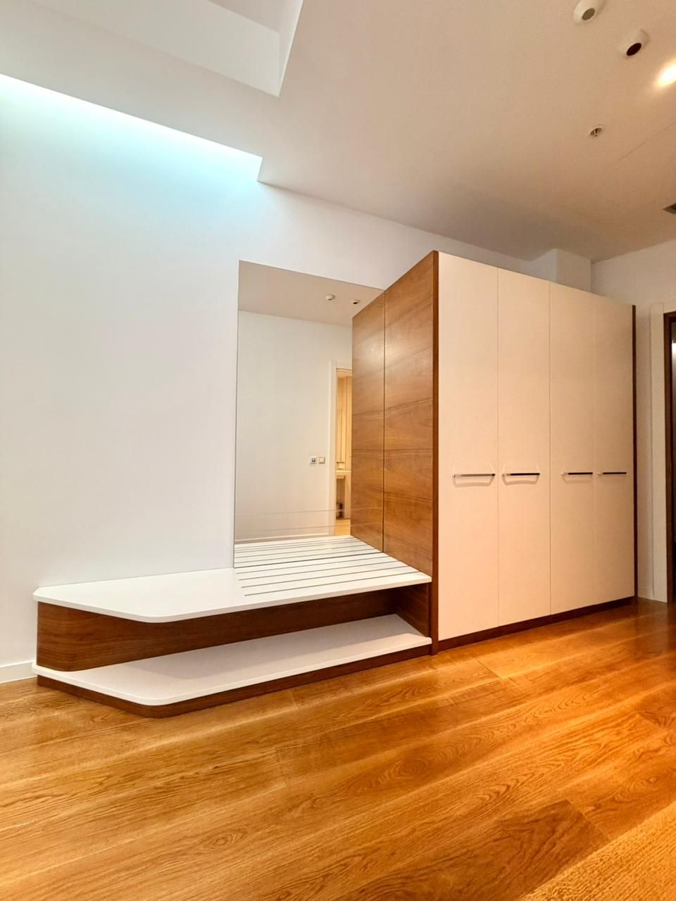 Ein modernes Zimmer mit Holzboden, einer eingebauten Sitzbank und einem großen Kleiderschrank mit mehreren Türen.